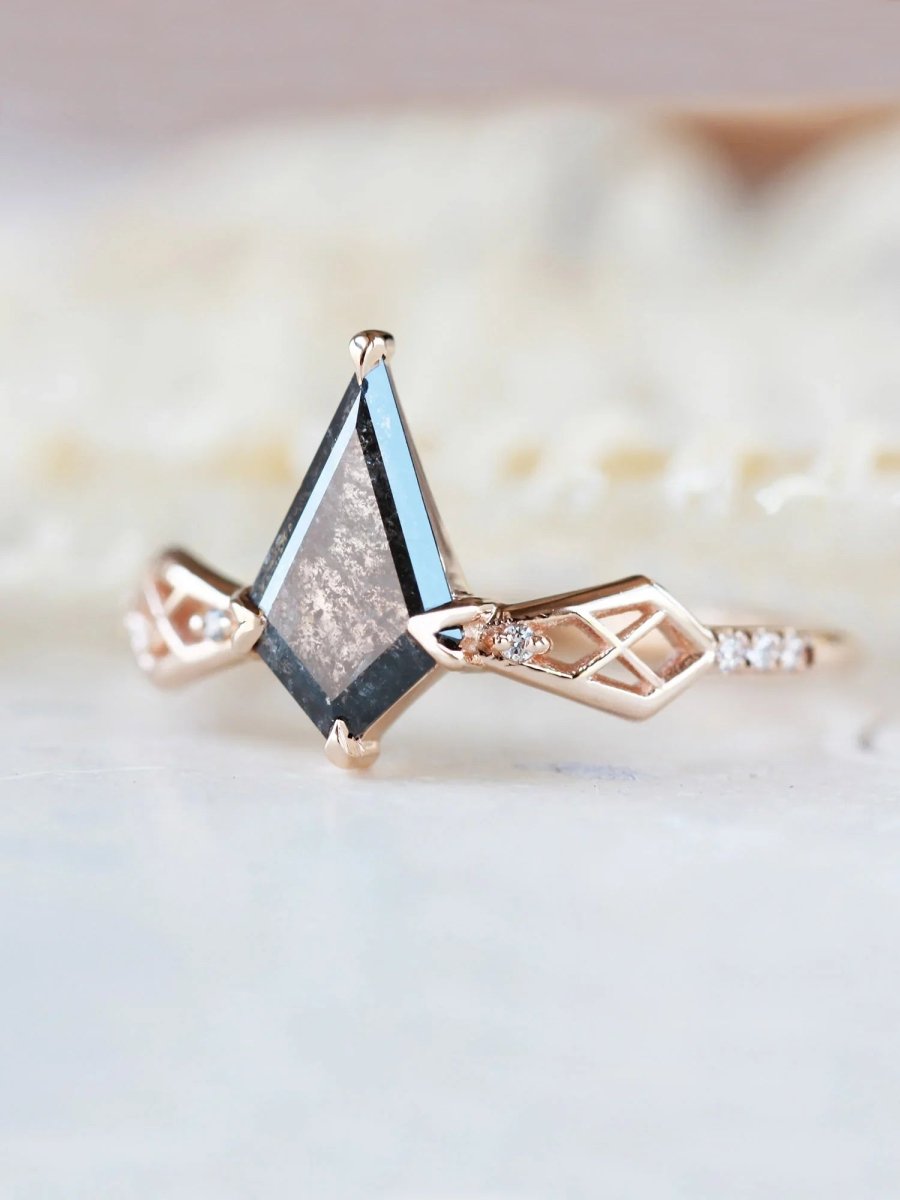 Close-up of 3/4 view of salt and pepper kite center stone on modern Art Deco kite engagement ring with latticed shoulders and melee diamonds out of focus