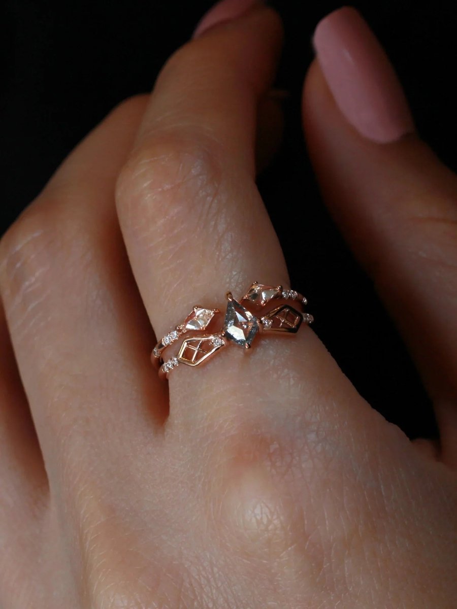 Dramatically lit close-up of finger wearing petite modern Art Deco kite ring with geometric lattice detailing stacked under kite open band
