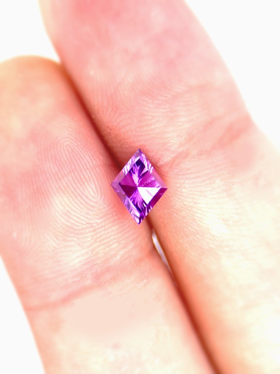 Purple sapphire held between two fingers against a white background for scale