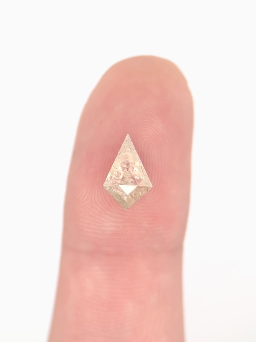 Loose kite-shaped yellow salt and pepper diamond with white inclusions, step cut, shown on fingertip for scale