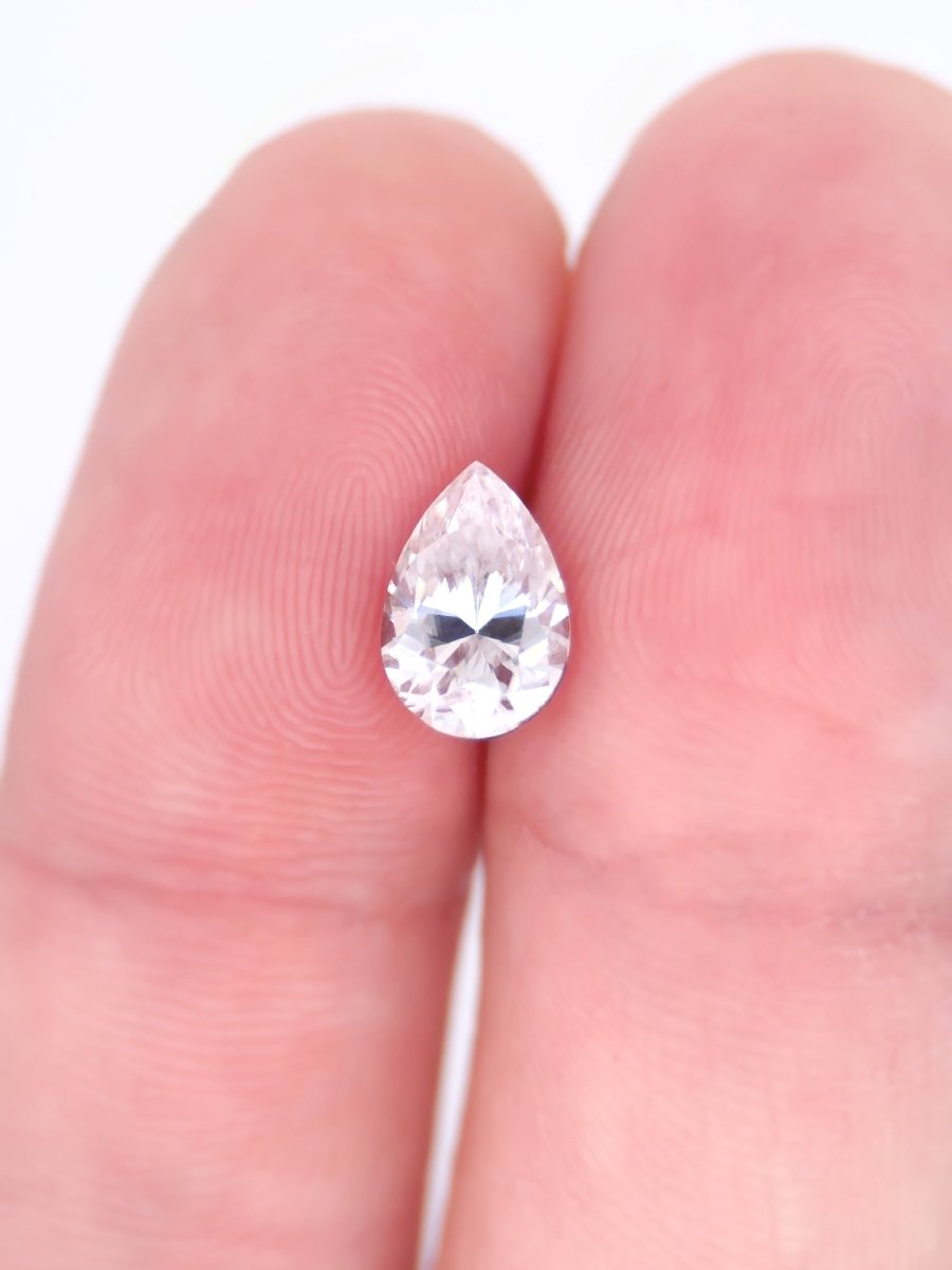 Pear-shaped diamond held between two fingers on a white background