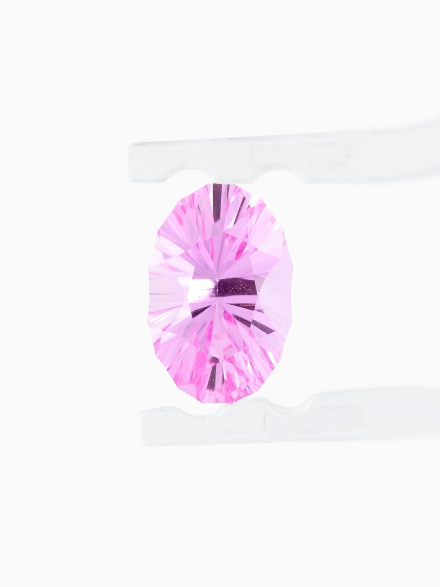 face view of designer cut pink oval sapphire held between tweezers on a white background