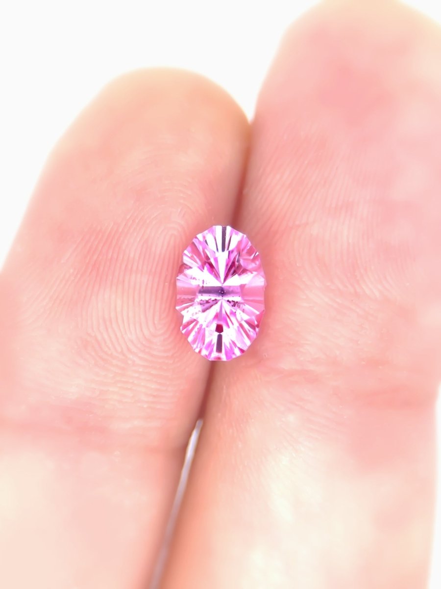 Pink sapphire oval held between two fingers on a white background for scale
