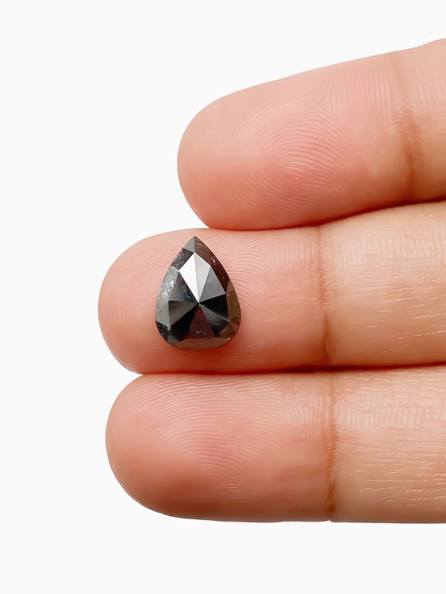 sustainable lab-grown pear shaped salt pepper diamond between fingers for scale