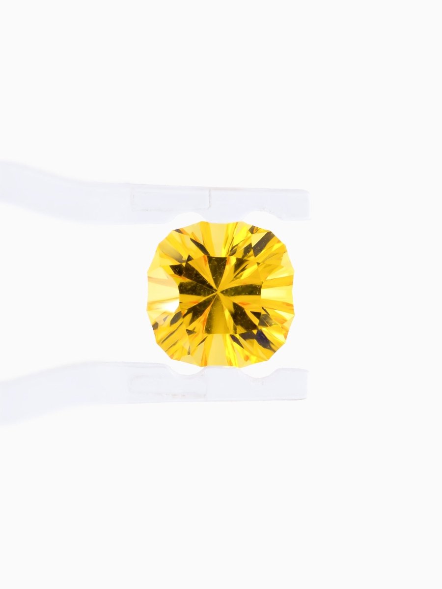 face view of designer cut yellow cushion sapphire held between tweezers on a white background