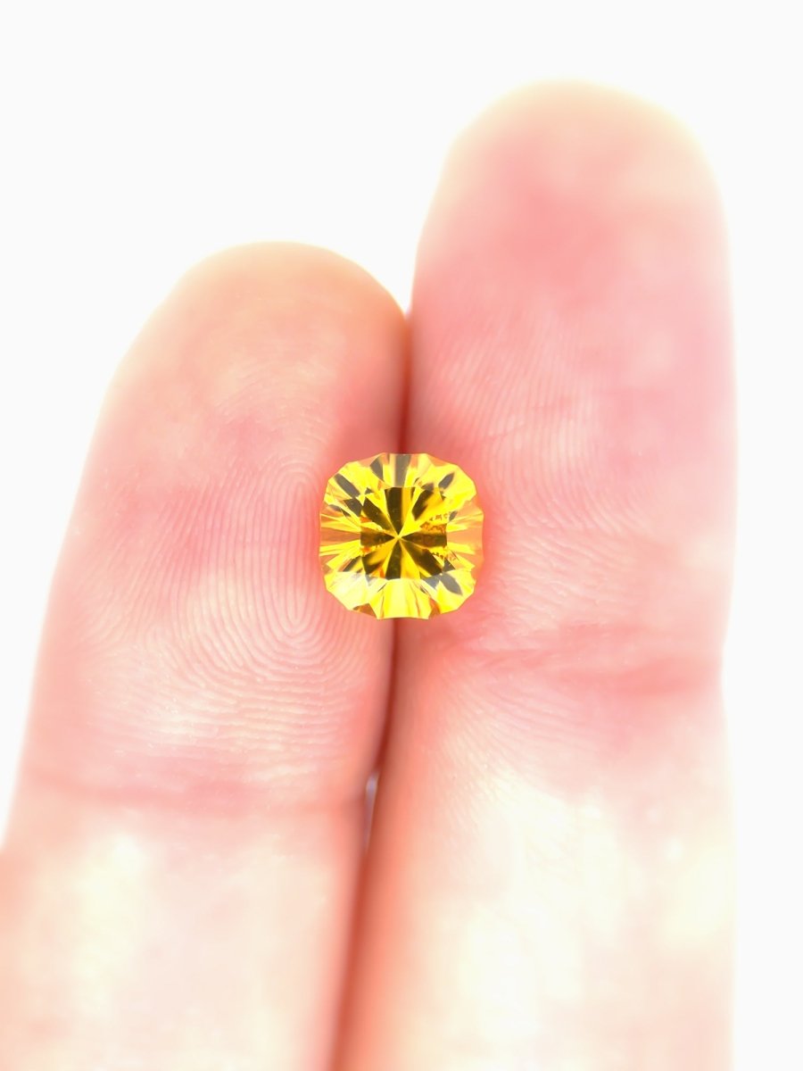 Yellow sapphire held between two fingers against a white background for scale