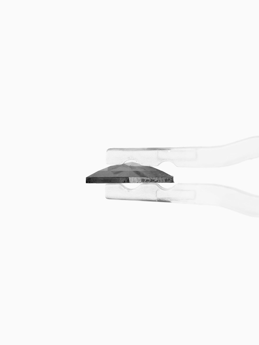 profile view of loose lab-grown hexagon salt pepper diamond gemstone held by tweezers
