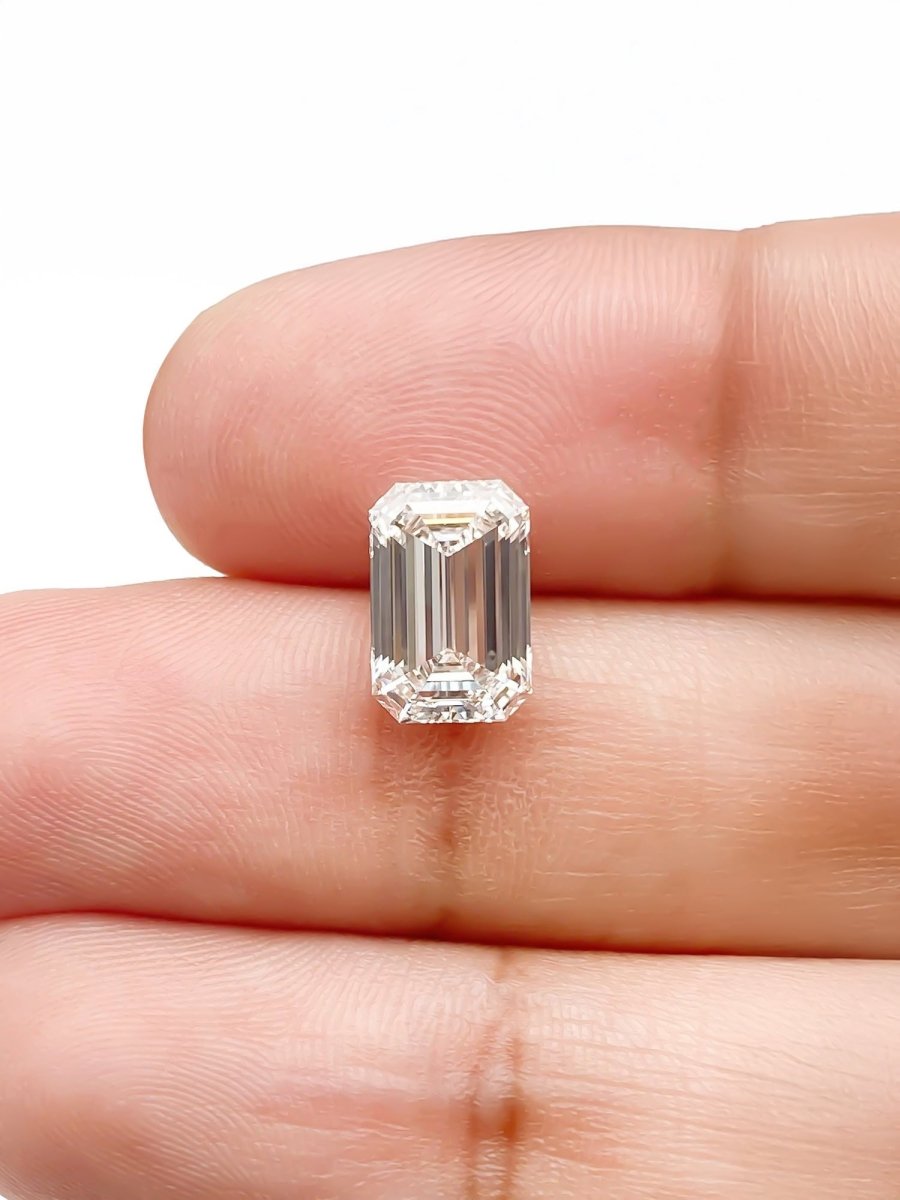 Emerald-cut diamond held between fingers on a white background for scale