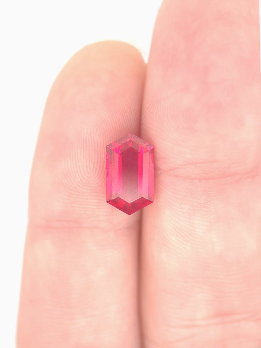 Pink gemstone held between fingers against a light pink background