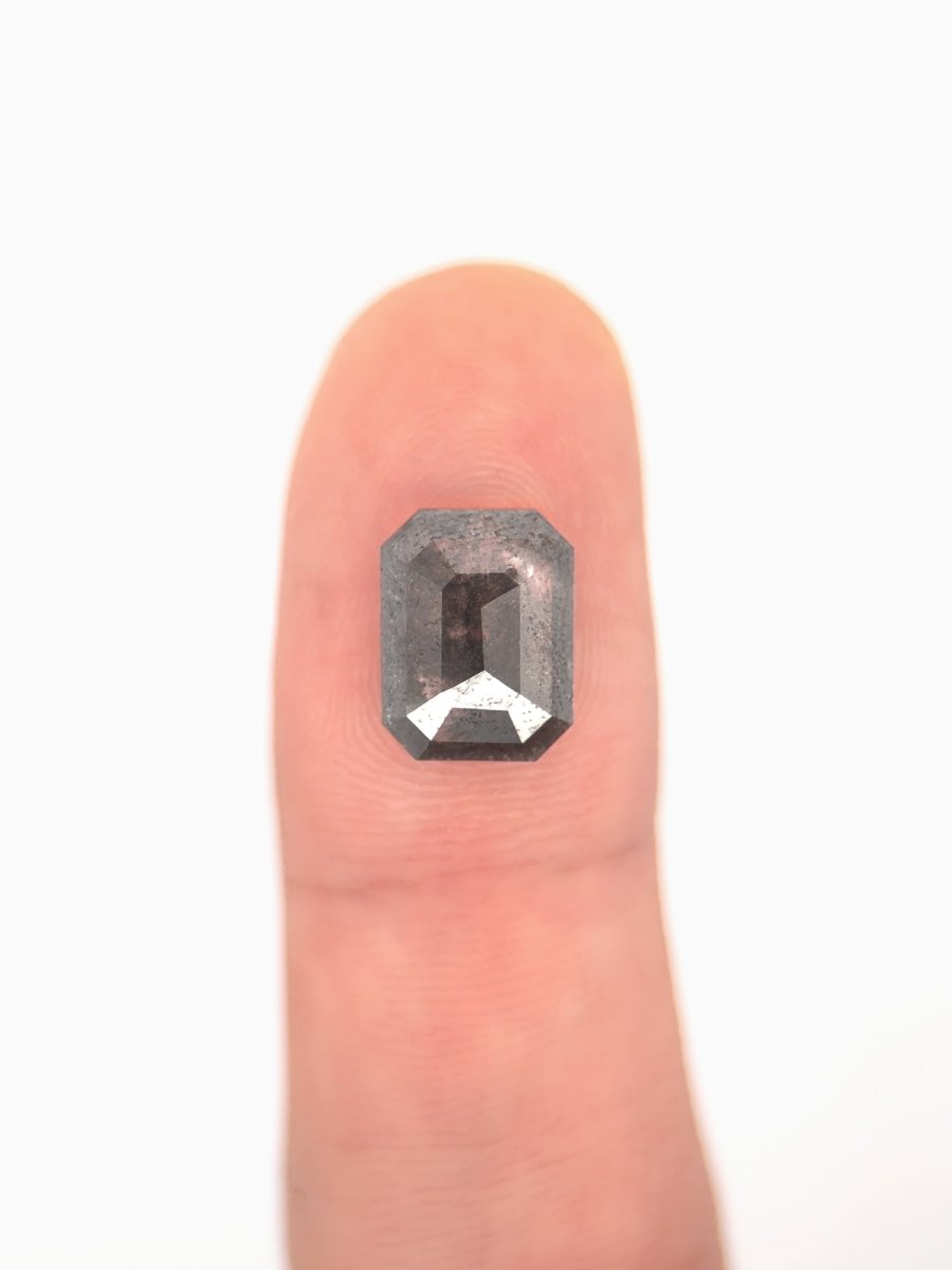 face view of loose lab-grown emerald-cut salt pepper diamond gemstone on finger for scale