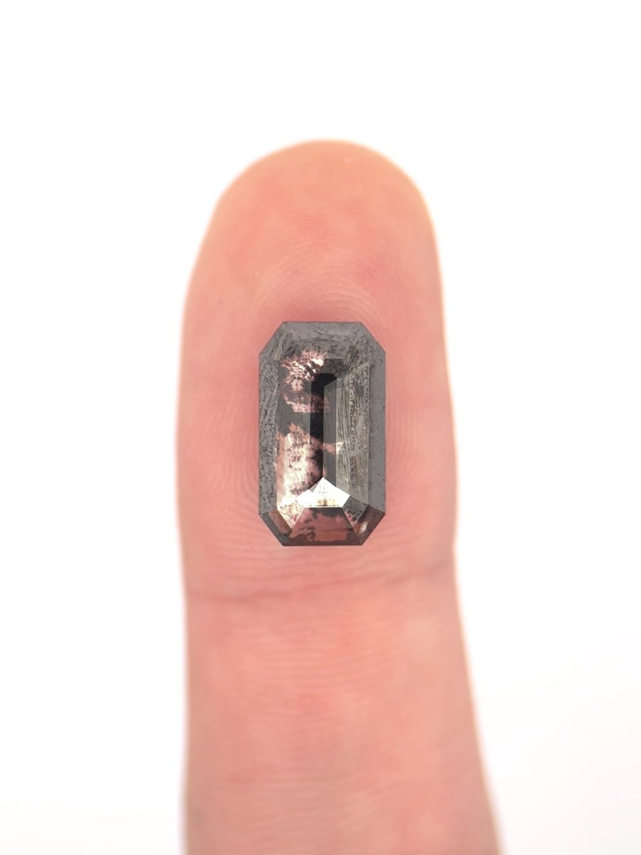 face view of loose lab-grown emerald-cut salt pepper diamond gemstone on finger for scale
