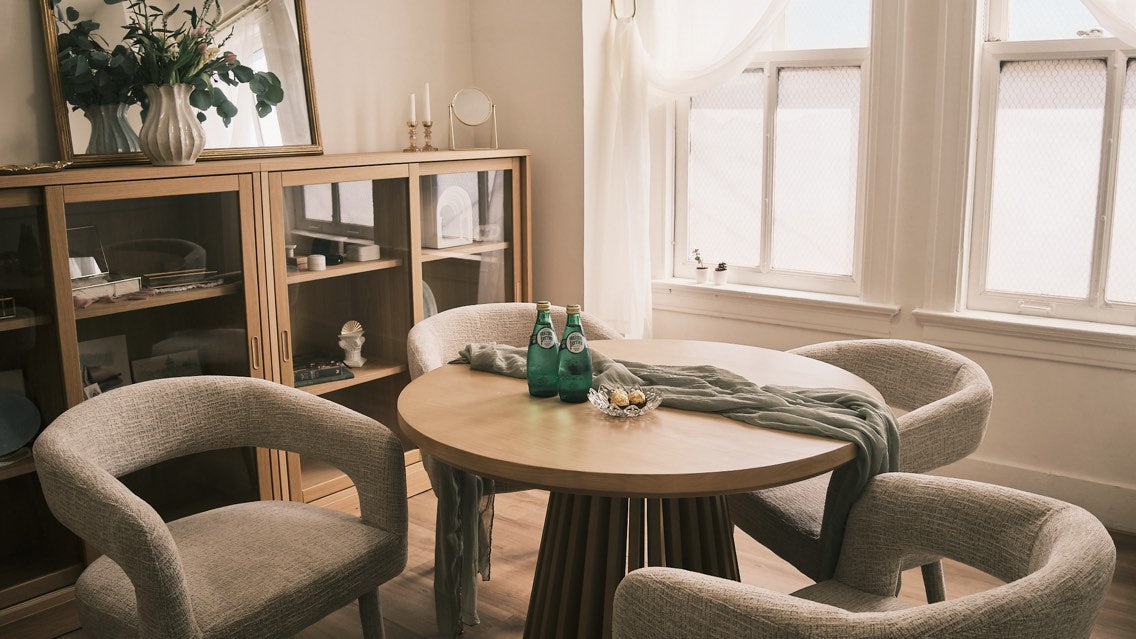 Round wooden table with four chairs in a room with large windows.