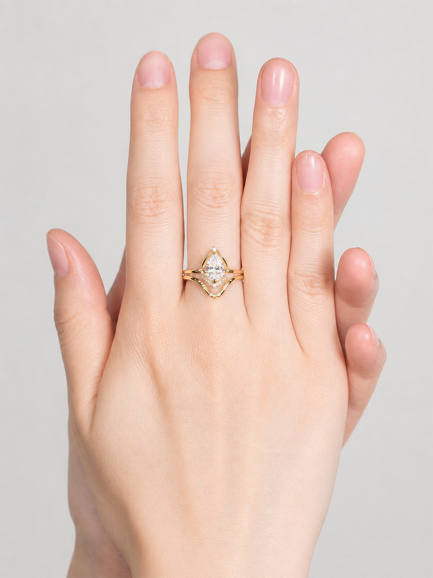 Gold ring with a diamond on a hand against a gray background pear engagement ring fine jewelry