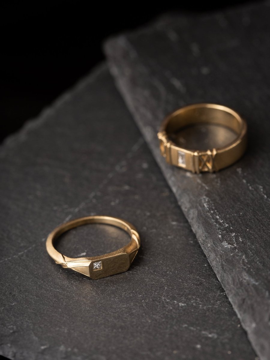 Two gold rings with diamond accents on a dark stone surface