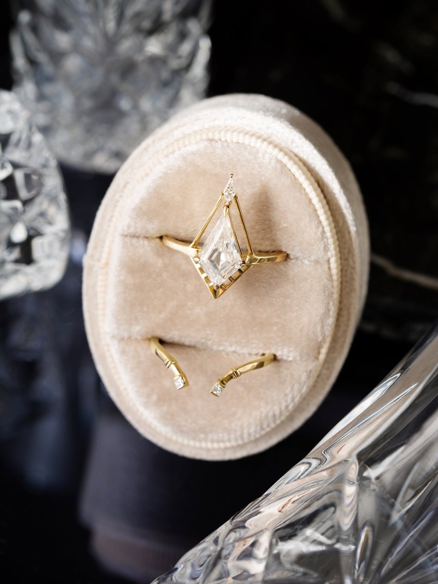 Gold Deco Kite Moissanite ring with a beige velvet box against a dark background