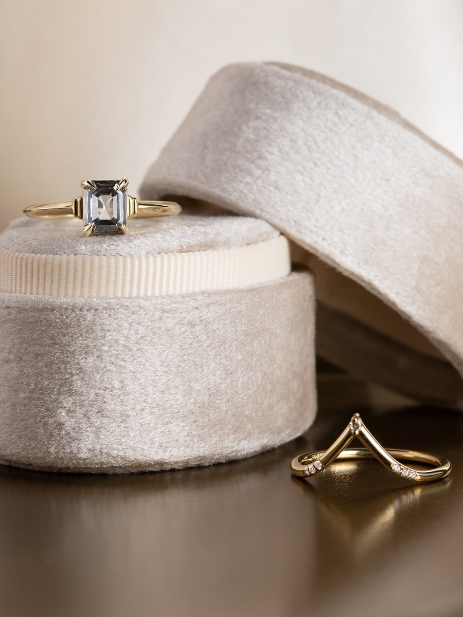 Gold ring with a diamond on a textured surface next to an open jewelry box.