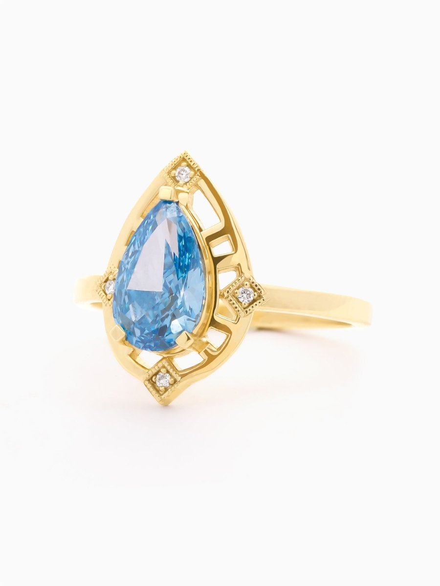 Three-quarter view of Ring showing glowing blue diamond above gold setting with vintage beadwork details.