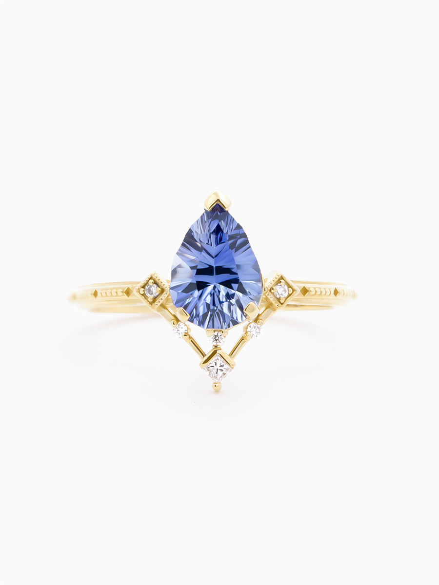 Art Deco–inspired ring with designer-cut blue pear and radiating detail on white background, face view