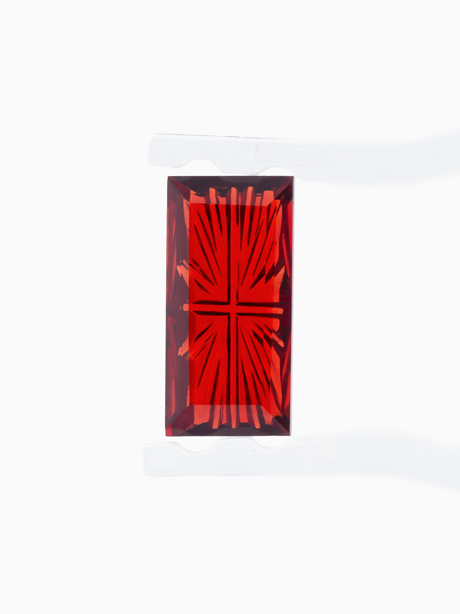 red garnet baguette with sunbursts cut into its pavilion held by tweezers, face view