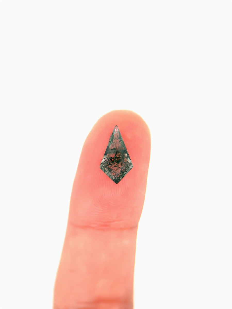 Kite-shaped loose moss agate gemstone with dendritic green inclusions on finger for scale