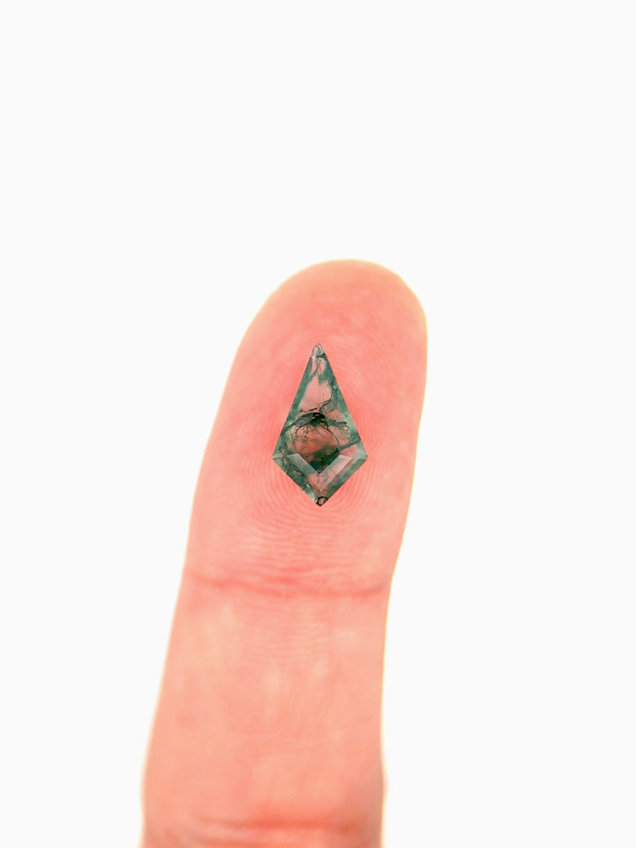Kite-shaped loose moss agate gemstone with dendritic green inclusions on finger for scale