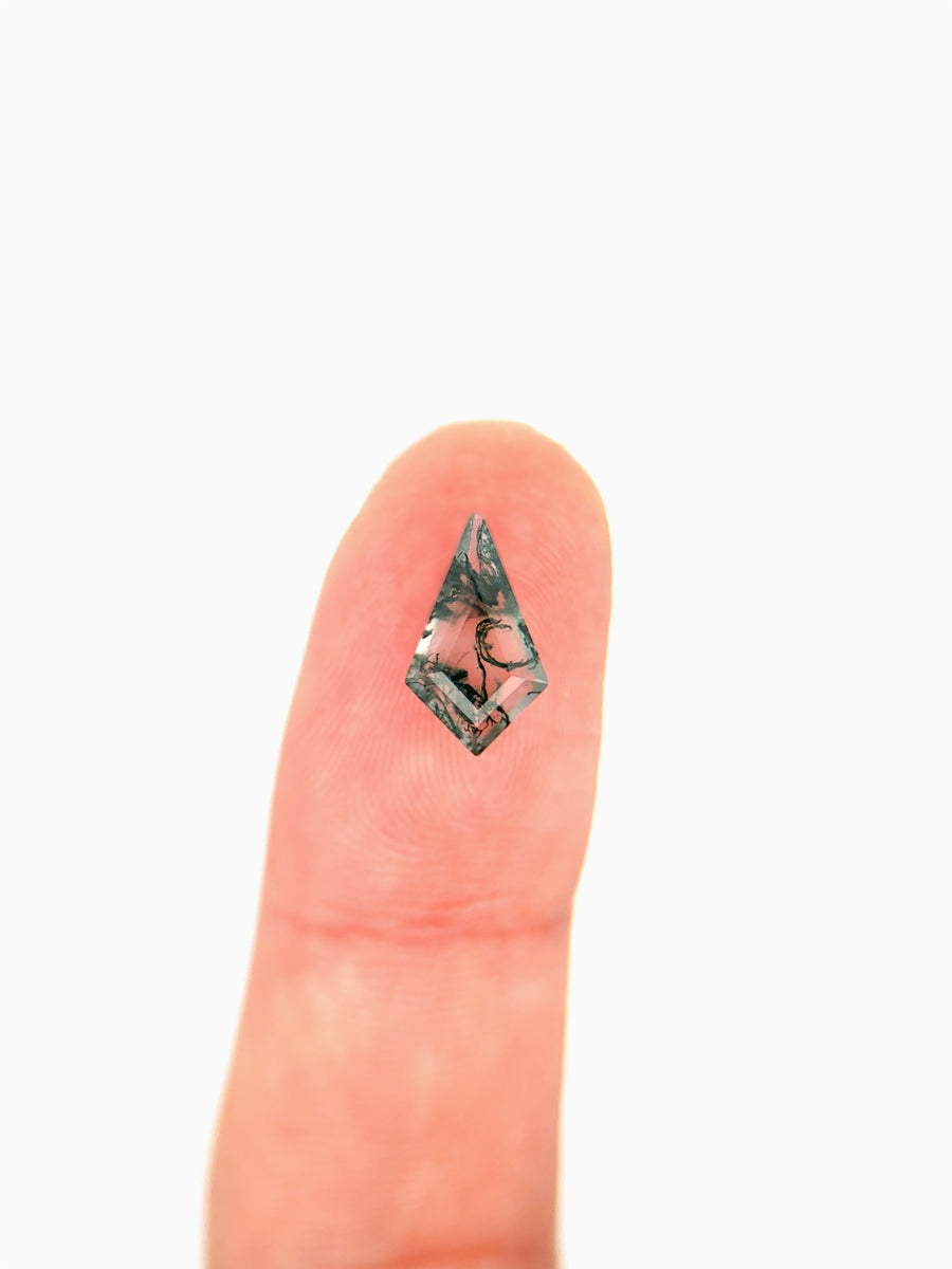Kite-shaped loose moss agate gemstone with dendritic green inclusions  on finger for scale