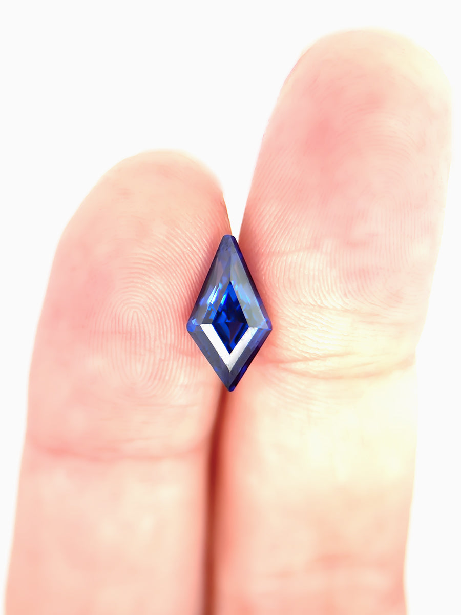 deep royal blue sapphire kite placed on finger for scale