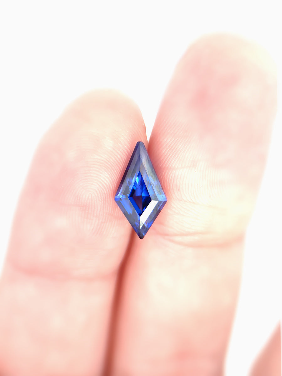 deep royal blue sapphire kite placed on finger for scale
