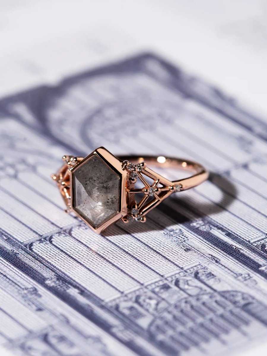 Rose gold ring with a large salt pepper diamond on architectural blueprints