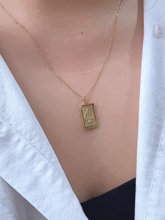 GIF of chest wearing rectangular playing card charm with embossed gold ace of spade illustration and birthstone accent