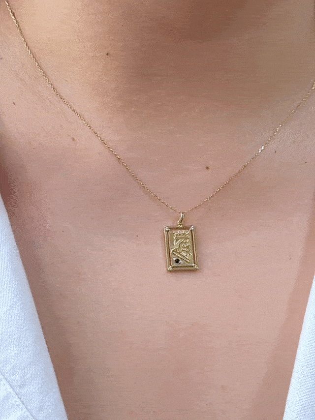 GIF of chest wearing rectangular playing card charm with embossed gold king illustration and birthstone accent