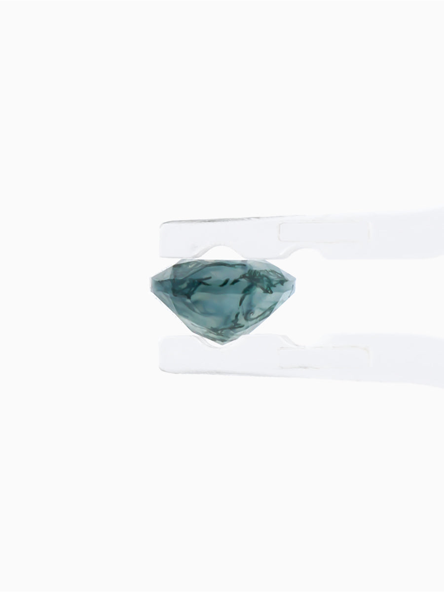 profile view of blue-green moss agate pear with dendritic inclusions held by tweezers to show thickness