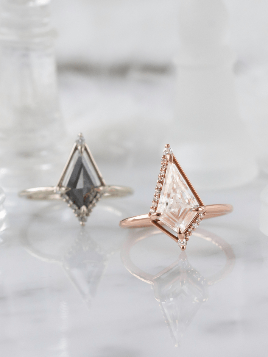 Two triangular gemstone rings, one in silver and one in rose gold, on a light background.