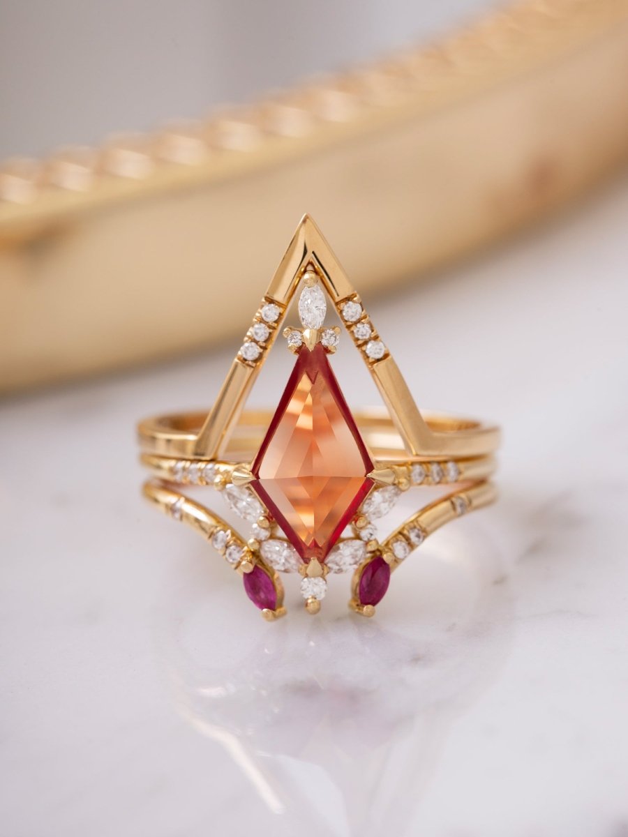 Gold ring with a large orange gemstone and smaller red gemstones on a marble surface.