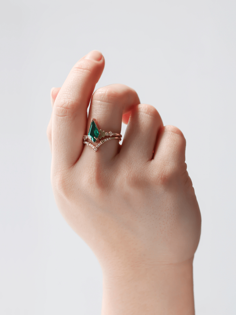 Art Deco engagement ring with kite emerald, stepped chevron shoulders, milgrain accents, and chevron band on hand