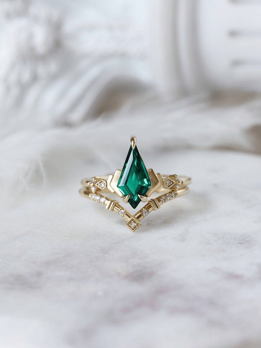 Face of Art Deco kite emerald ring with chevron band, set against soft classical white columns that evoke an ethereal, timeless feel