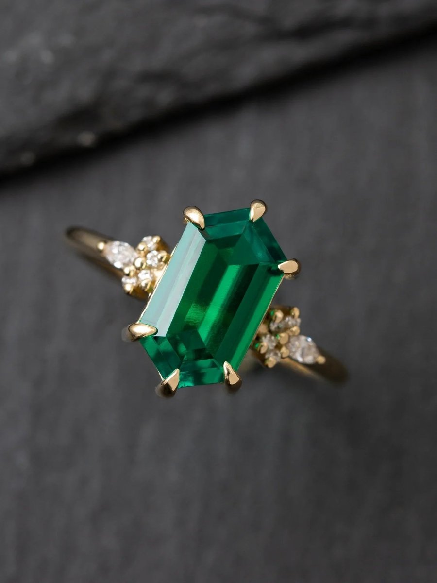 Gold ring with a large emerald-cut green gemstone on a dark background