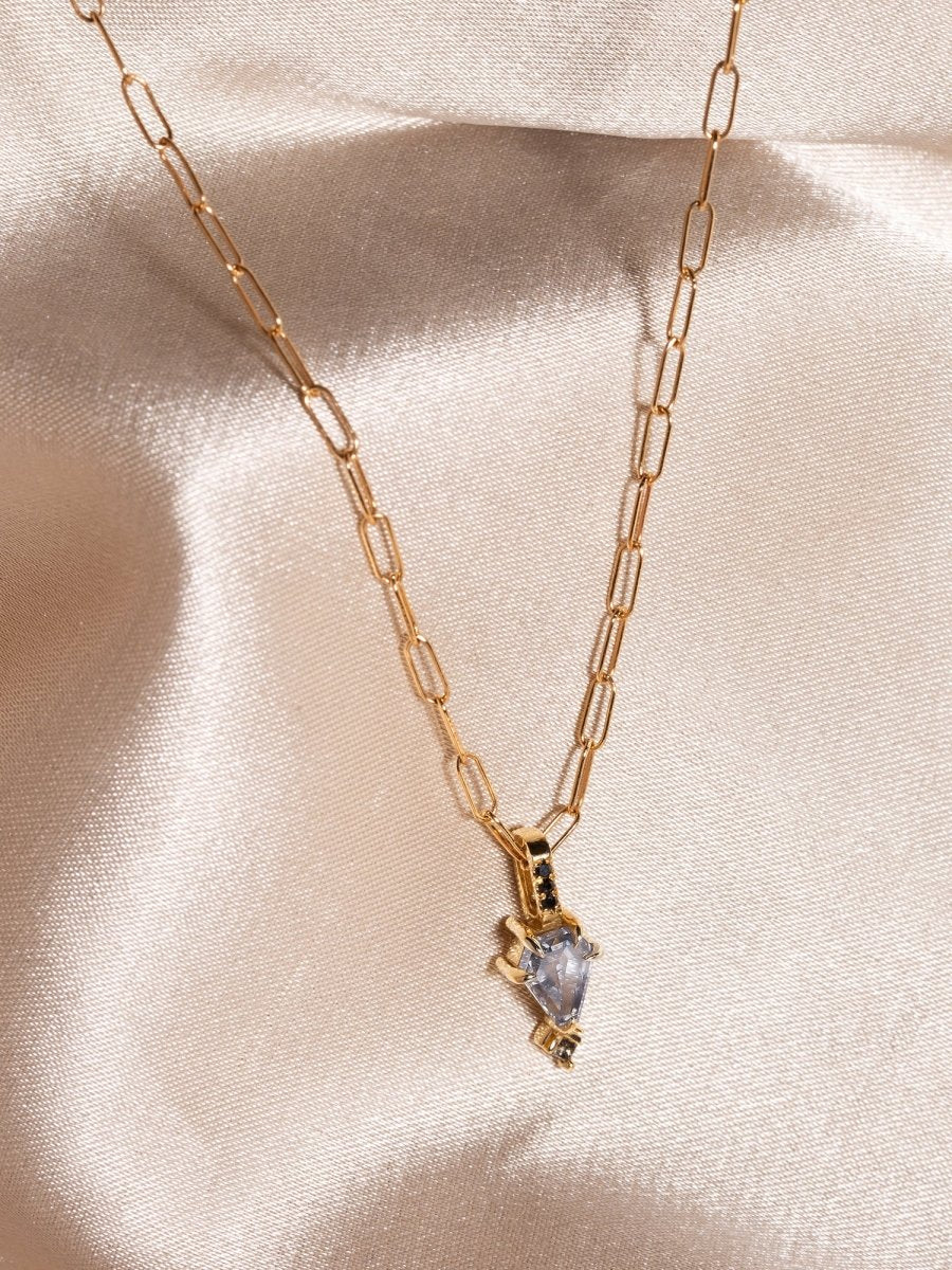 Gold necklace with a heart-shaped diamond pendant on a beige satin background