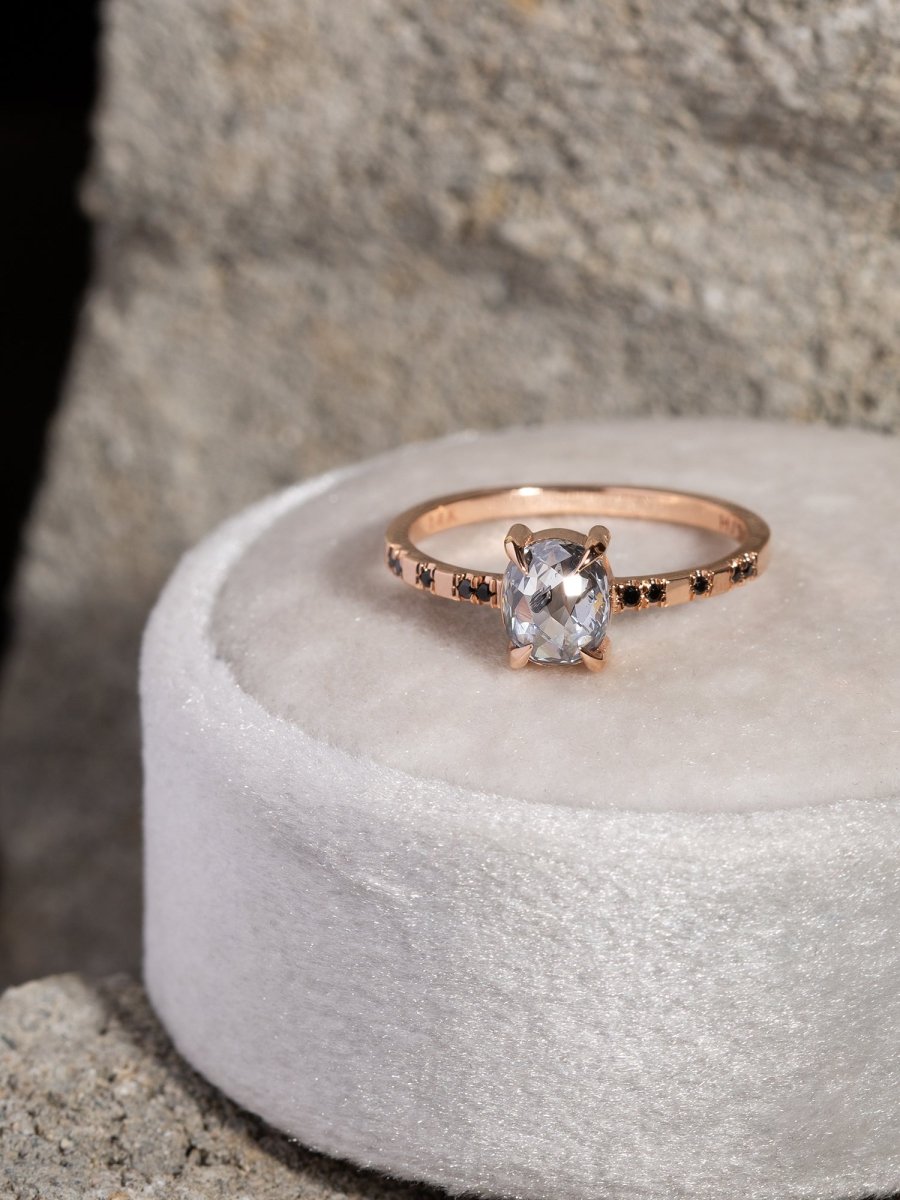 Rose gold ring with a clear gemstone on a white cushion against a stone background