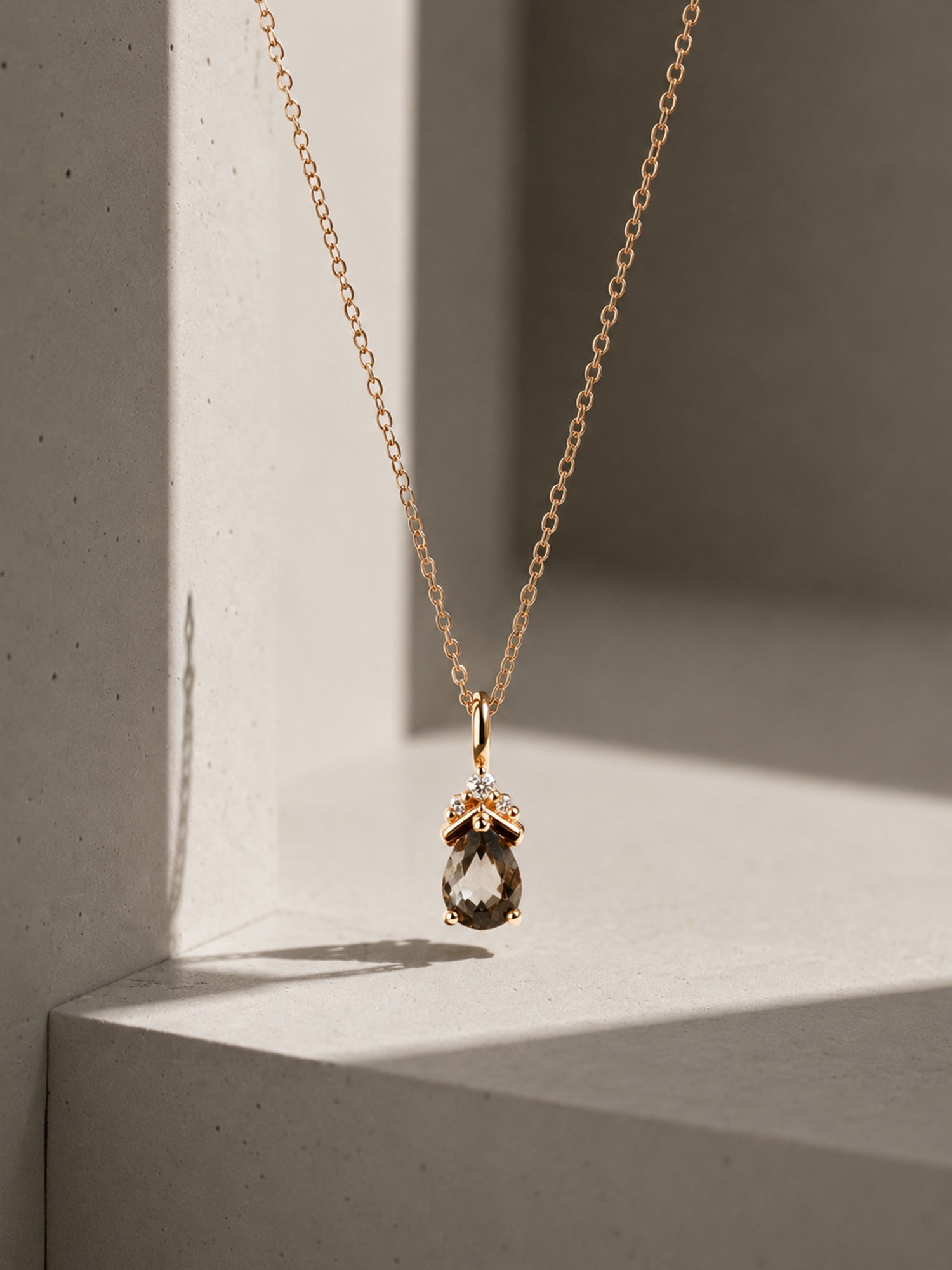 Gold necklace with a teardrop-shaped pendant on a neutral background