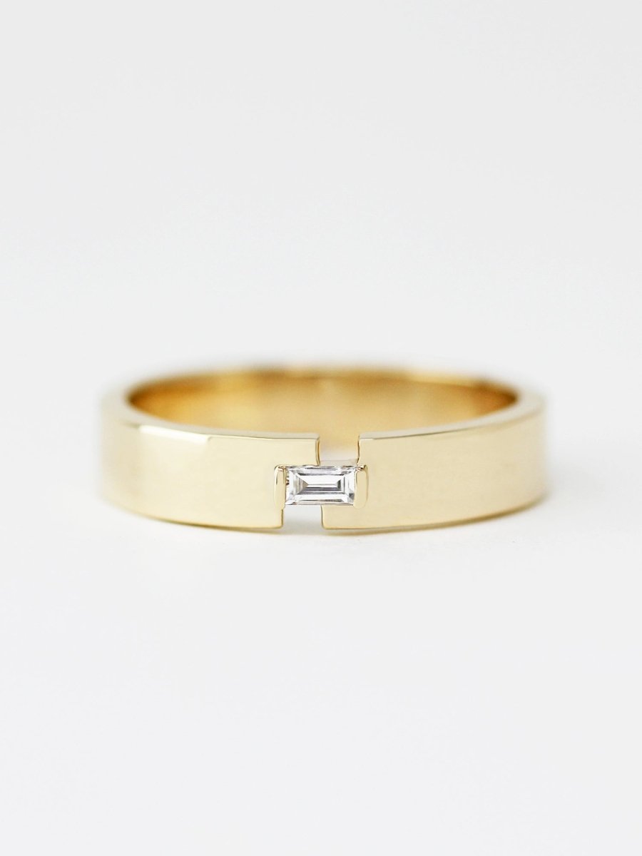 A gold-colored band ring with a baguette diamond set in the center.