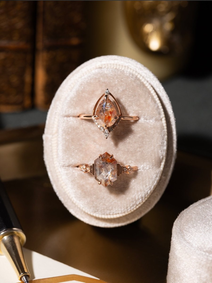 Two rose gold rings with gemstones on a beige velvet cushion.