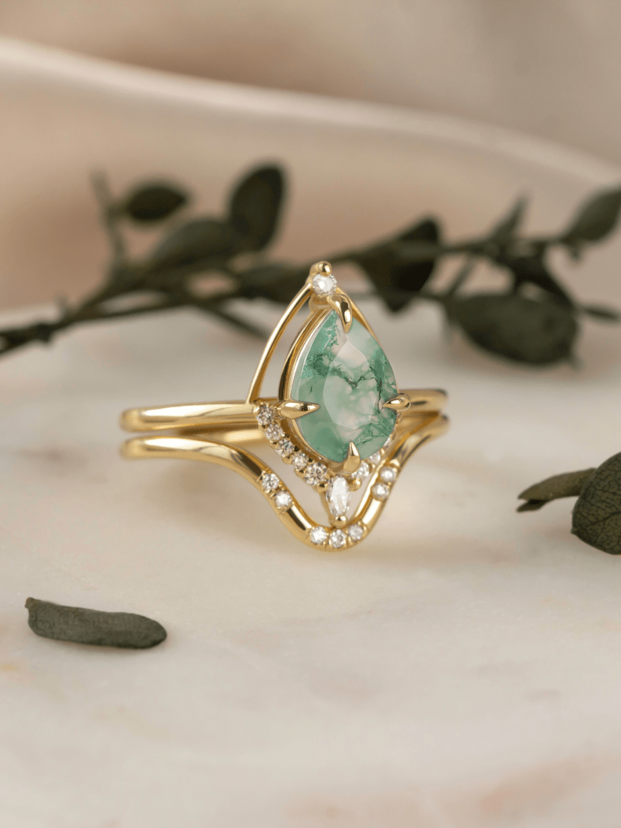 Gold ring with a green gemstone on a marble surface with leaves