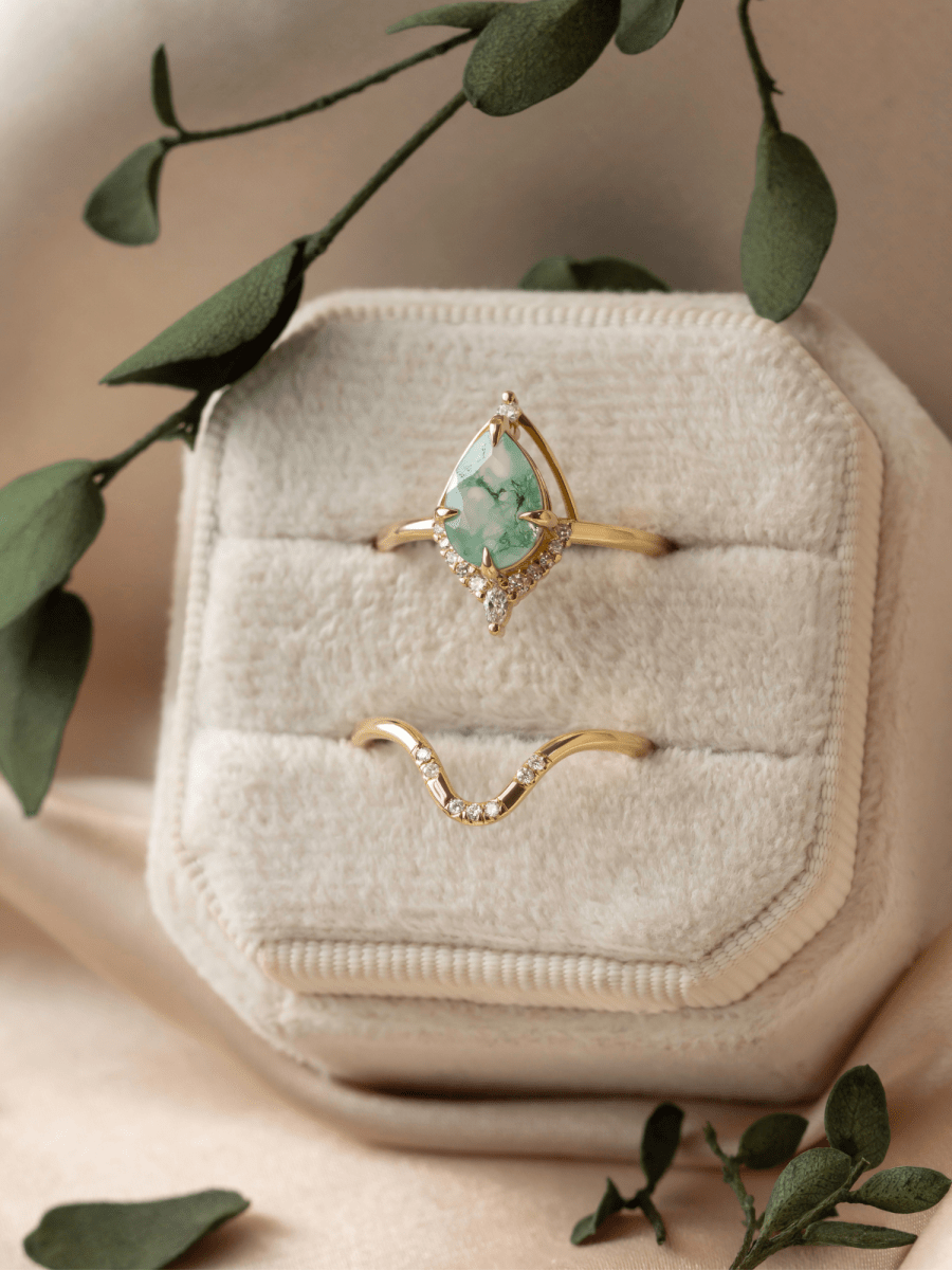 Gold ring with a green gemstone in a jewelry box with green leaves around
