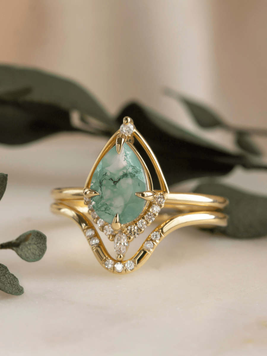 Gold ring with a green gemstone and diamond accents on a neutral background