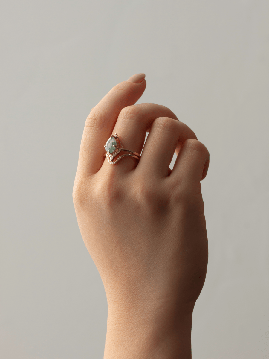 Hand wearing a gold ring with a green gemstone on a neutral background