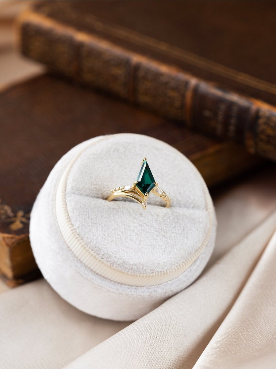 Gold ring with a green gemstone in a white jewelry box on a wooden surface.