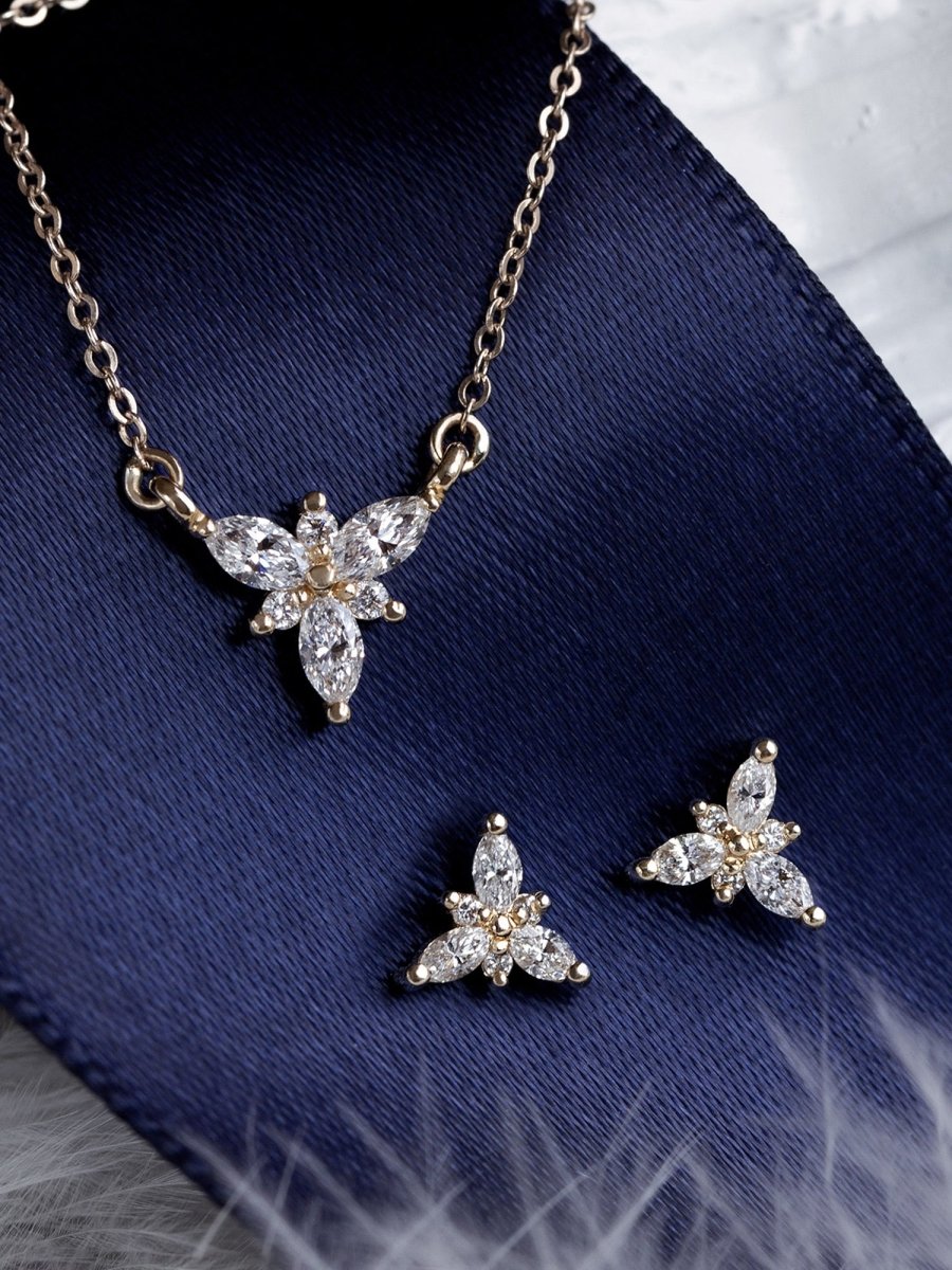 A set of jewelry including a necklace, ring, and band, featuring white marquise and round diamonds, displayed against a blue background.