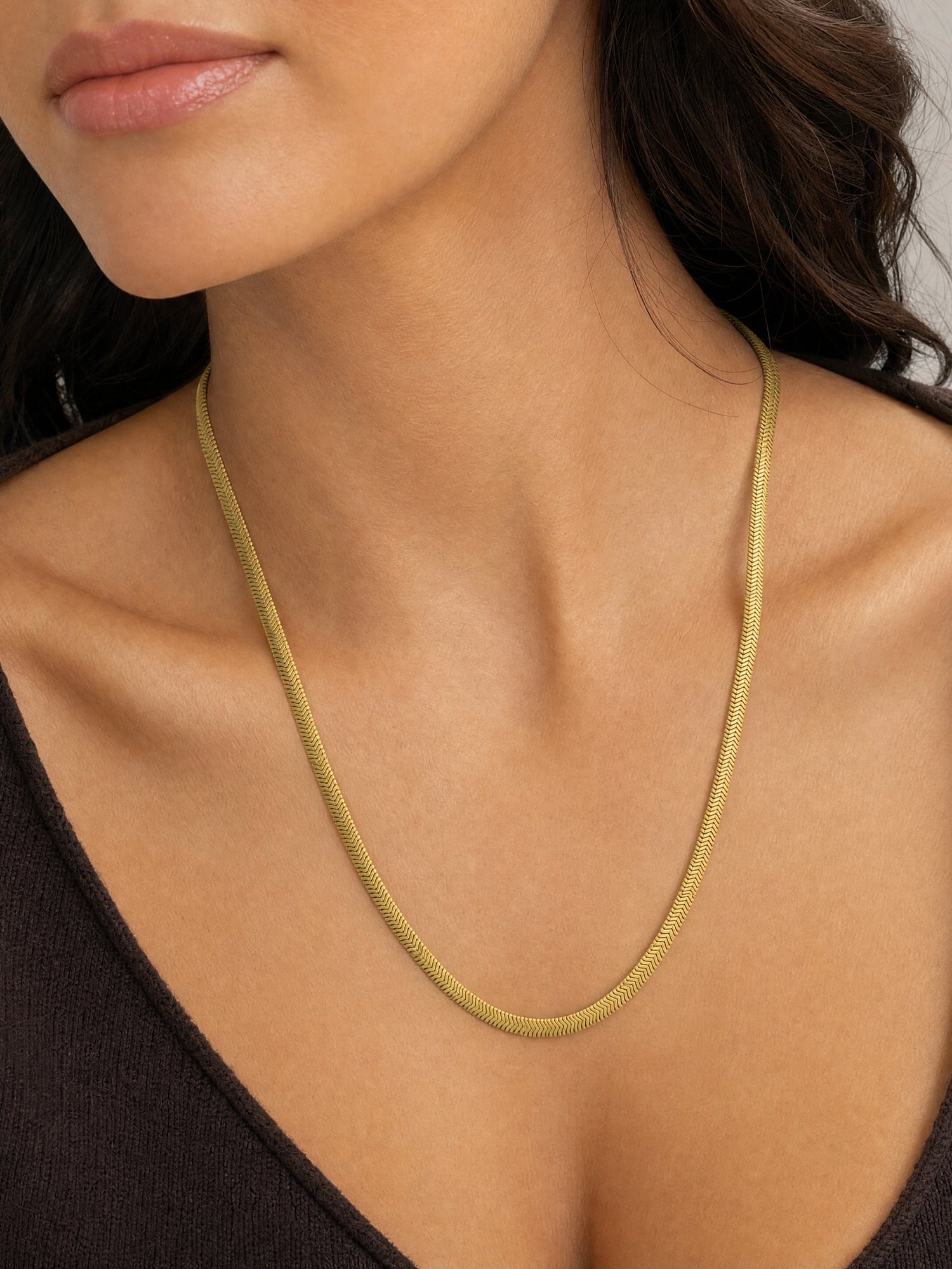 A close-up of a model wearing a delicate gold snake chain necklace, showing the necklace draped around her neck and collarbone.