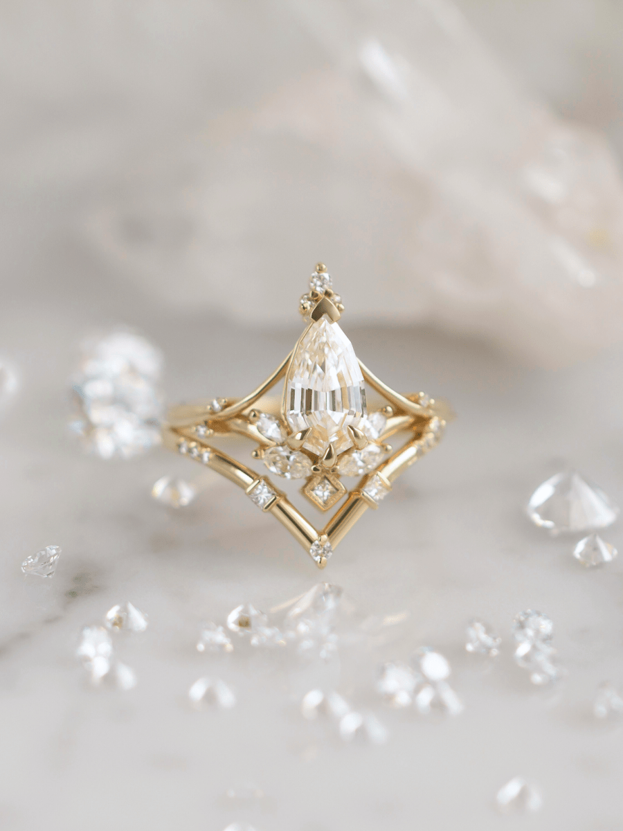 Art Nouveau split-shank engagement ring with marquise diamond, milgrain accents, and chevron band on marble, surrounded by loose stones